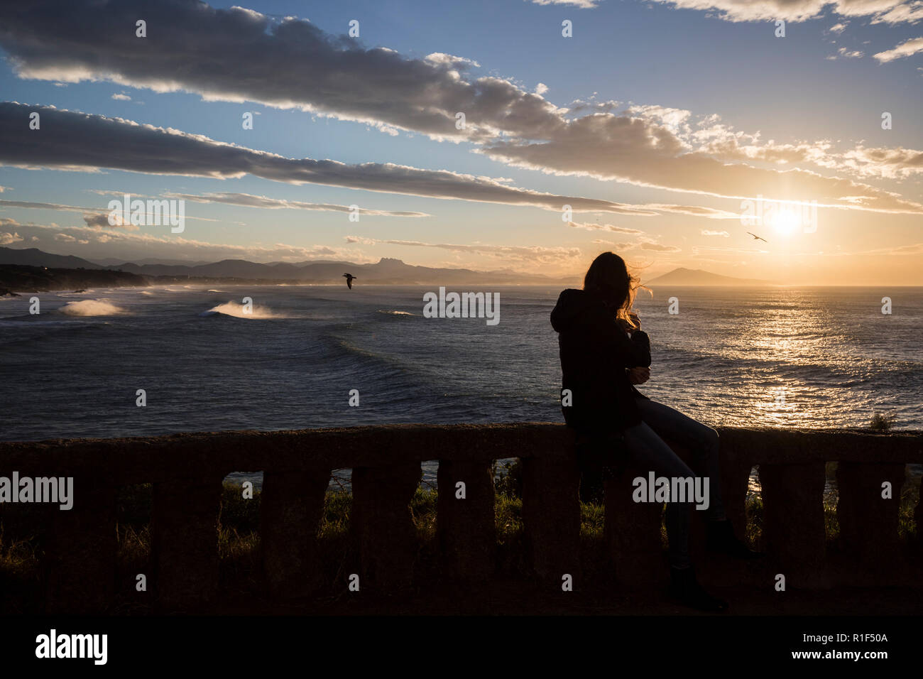 Donna seduta su una parete affacciata sull'oceano Atlantico al tramonto. Foto Stock