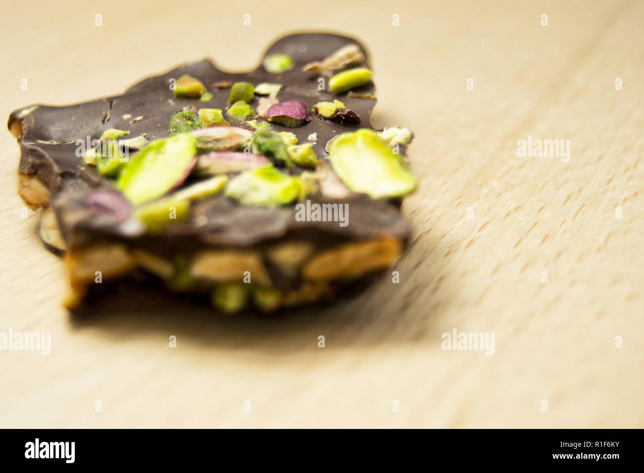 Gustosa barretta di cioccolato fondente con pistacchi e nocciole su un tagliere di legno Foto Stock