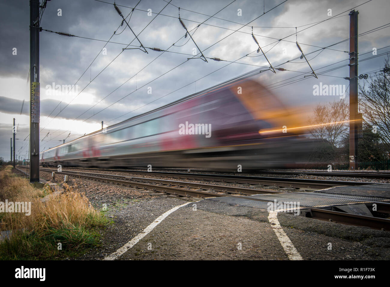 Un treno passeggeri passando la telecamera ad alta velocità e con un piede di attraversamento. Le nuvole scure nel cielo di aggiungere al dramma della scena. Foto Stock