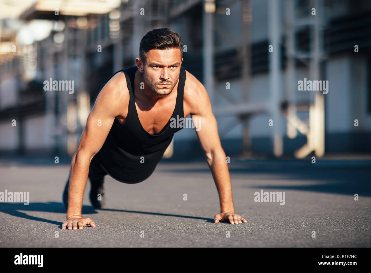 Grave giovane uomo che fa pushups all'esterno sul background industriale. concentrata sportivo facendo esercizio all'aperto Foto Stock