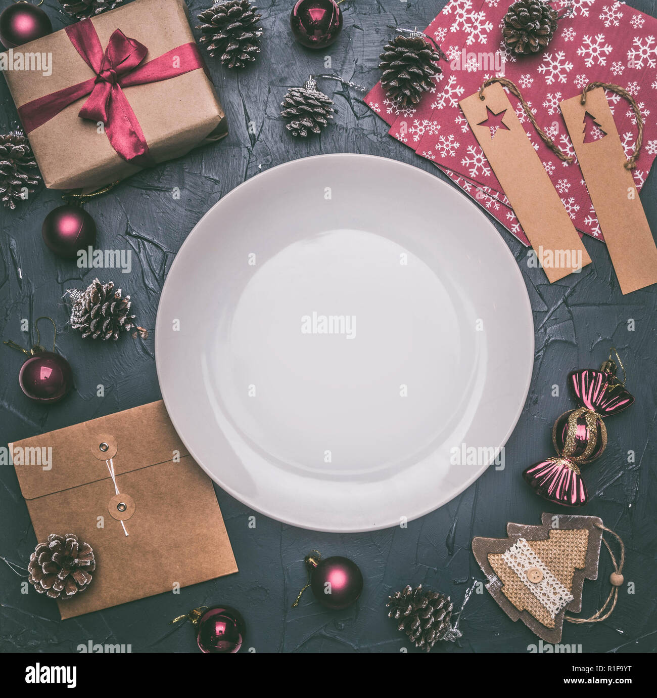 Concetto di natale, cartolina, confezione regalo giocattoli di Natale e coni, su uno sfondo grigio, foderata attorno ad una piastra bianca Foto Stock