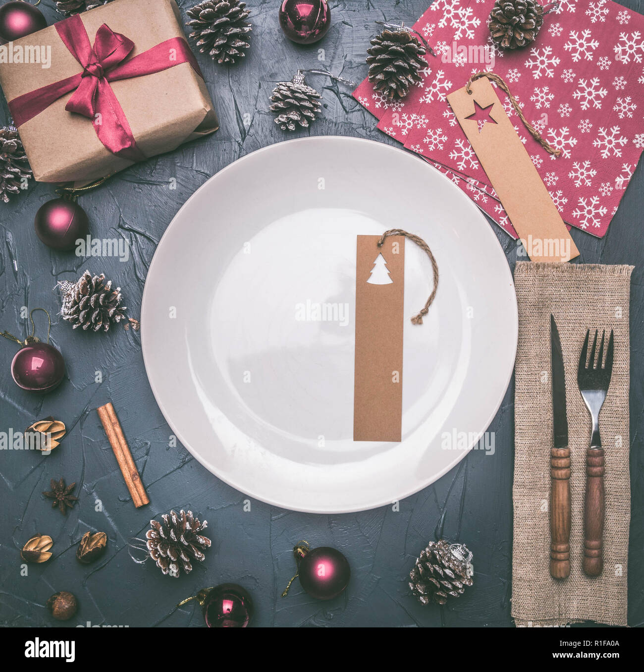 Concetto di natale, cartolina, confezione regalo giocattoli di Natale e coni, su uno sfondo grigio, foderata attorno ad una piastra bianca Foto Stock