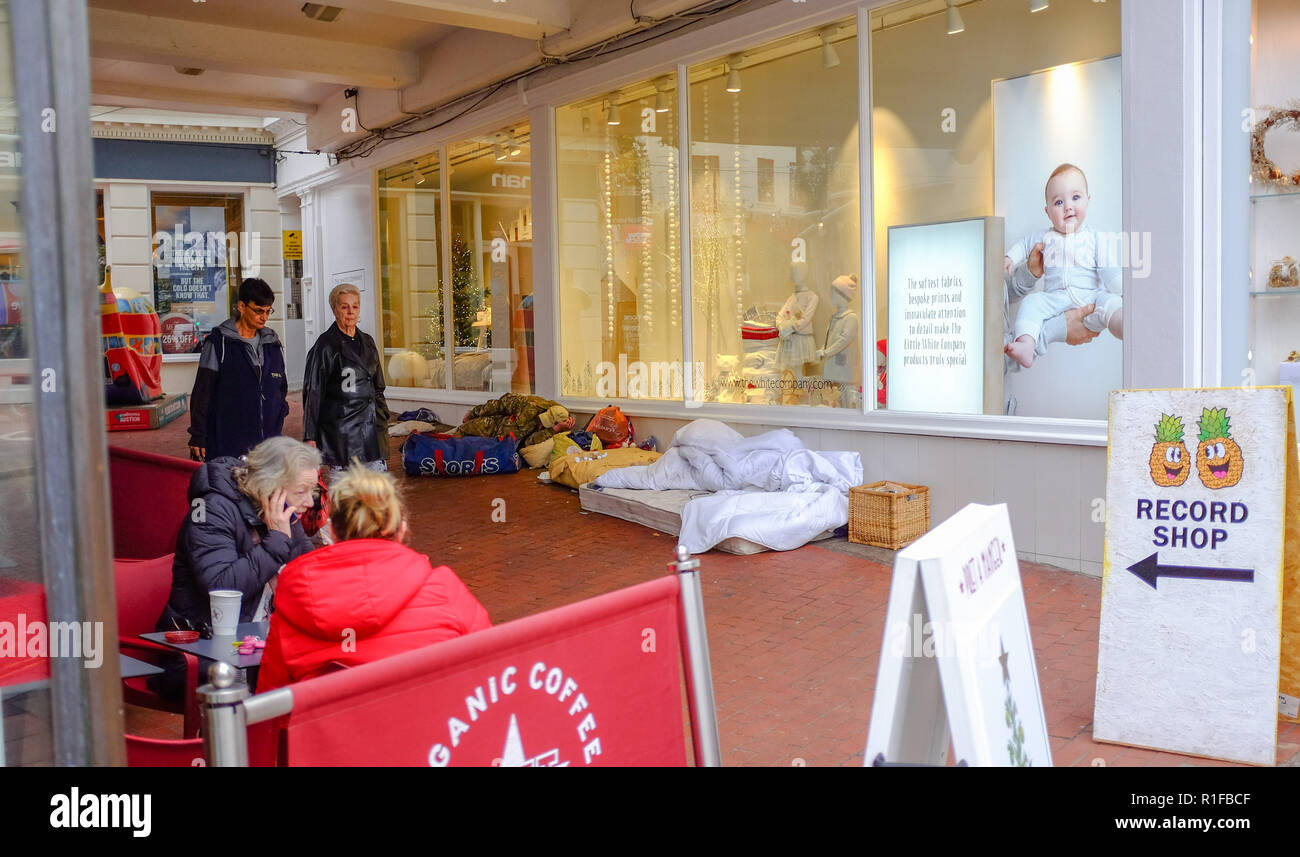 La persona senza dimora addormentato in negozio porta e finestra in shopping arcade come acquirenti passano a Brighton Regno Unito Foto Stock