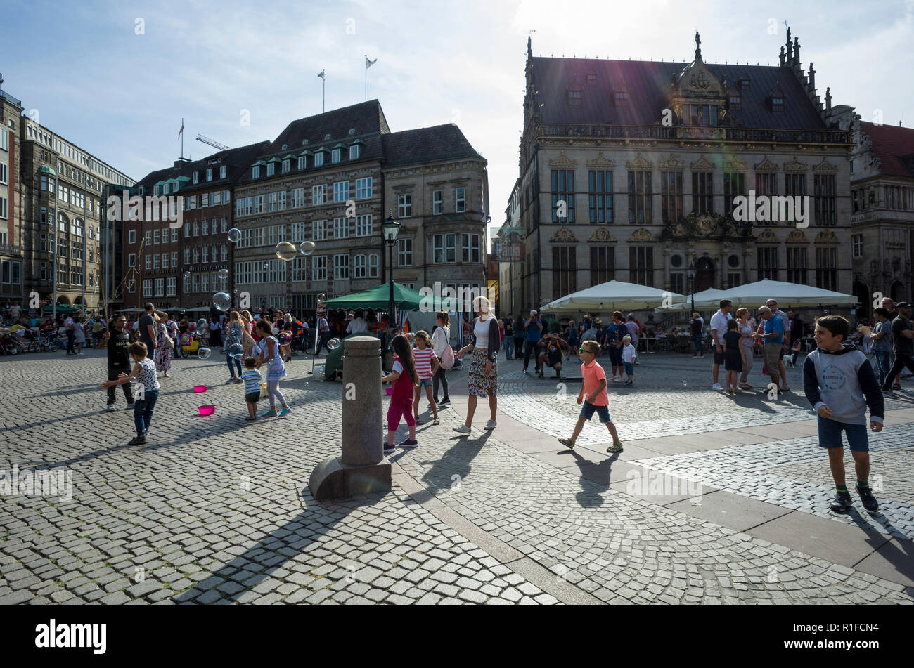 Marktplatz, Bremen. Deutschland La Germania. Una scena che si affaccia su piazza del mercato dove i bambini vengono intrattenuti da un uomo la creazione di bolle di grandi dimensioni che sono fluttuanti nell'aria. Si tratta di una luminosa giornata di sole e il sole è causando lunghe ombre per essere espressi dalle persone in scena. Foto Stock