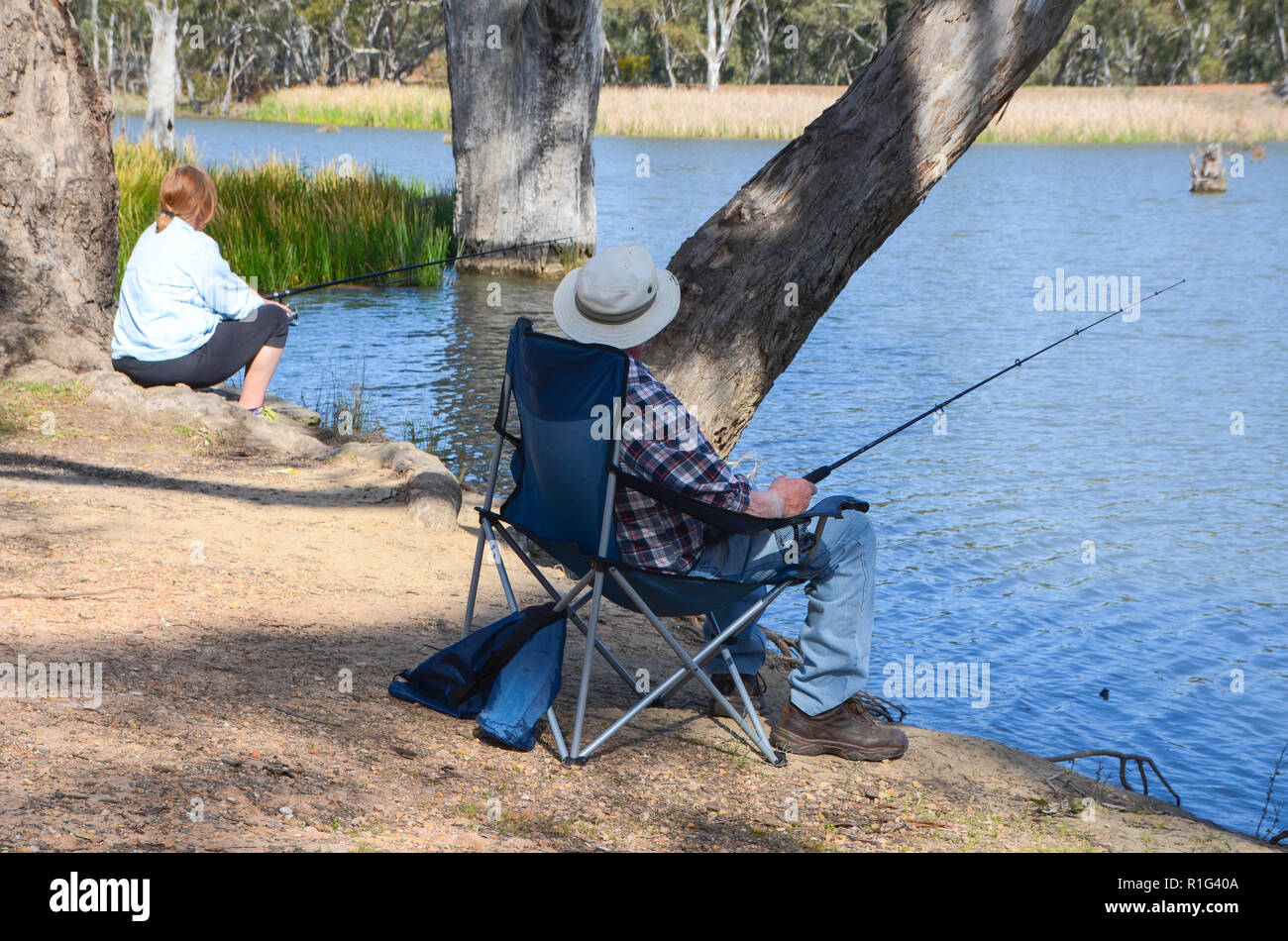Coppia maschio e femmina di sedersi sulla banca del fiume di pesca. Adulto anglers godere un momento di relax di pesca. Foto Stock