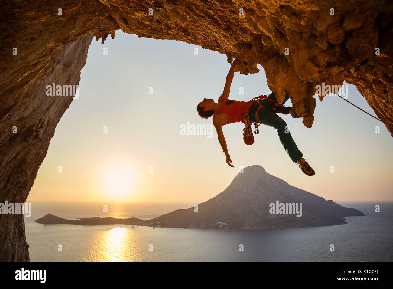Maschio di rocciatore appeso con una mano sul percorso impegnativo su roccia al tramonto Foto Stock