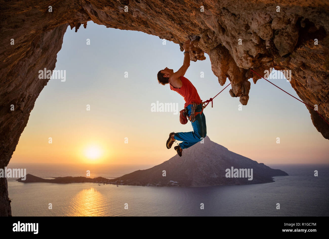 Maschio di rocciatore appeso con una mano sul percorso impegnativo su roccia al tramonto Foto Stock