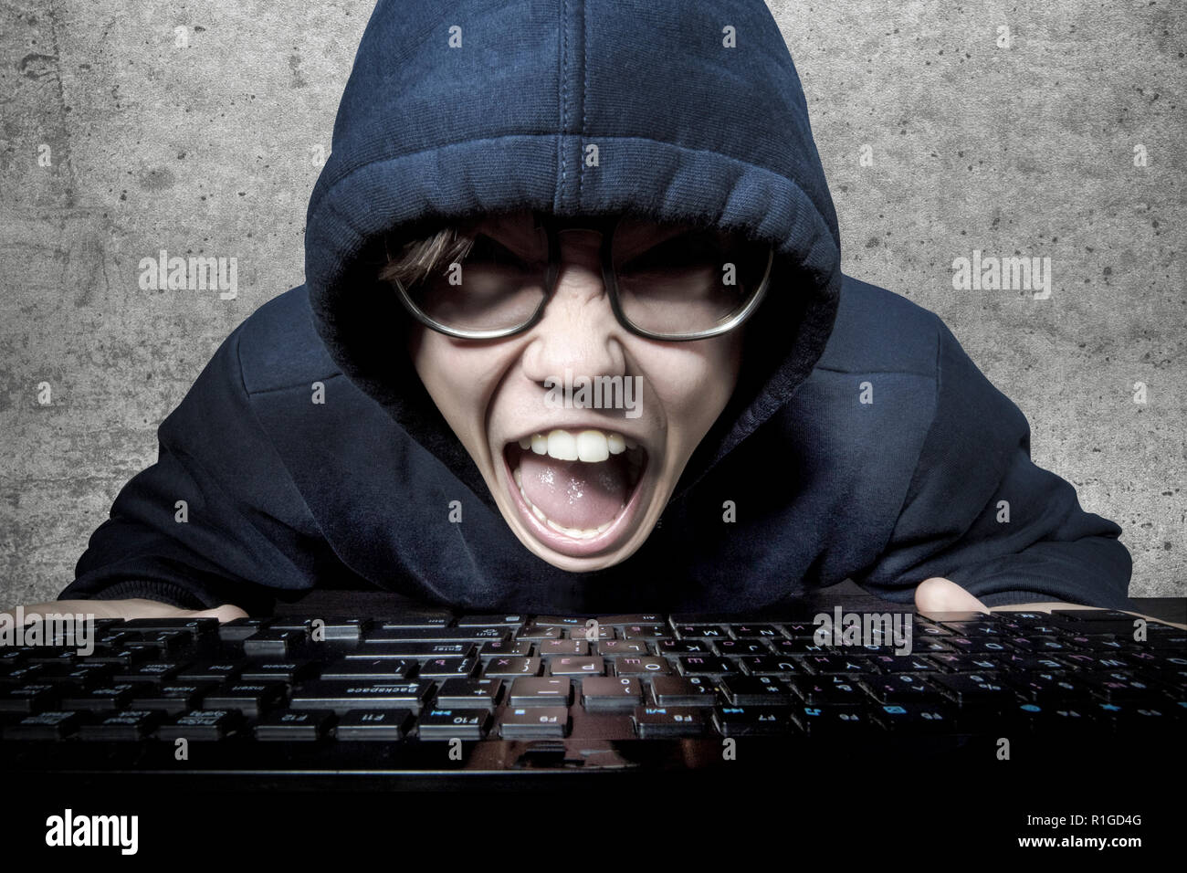 Hacker nel cofano e bicchieri urlando furiosamente seduto davanti alla tastiera Foto Stock