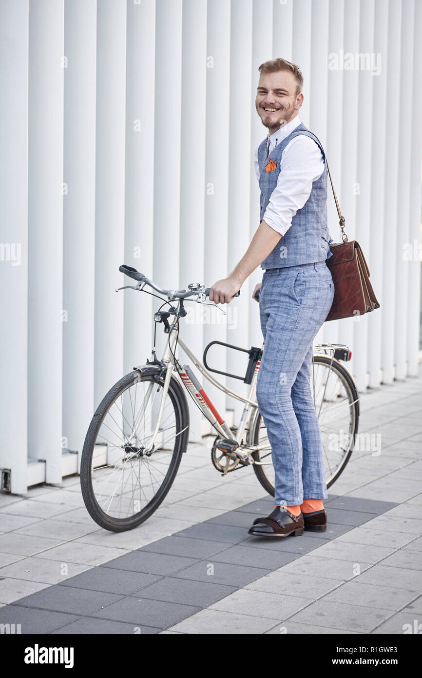 Un giovane uomo, 20-29 anni, indossa una tuta hipster, smart casual,  tenendo old city bike. moderno e bianco edificio a parete dietro Foto stock  - Alamy