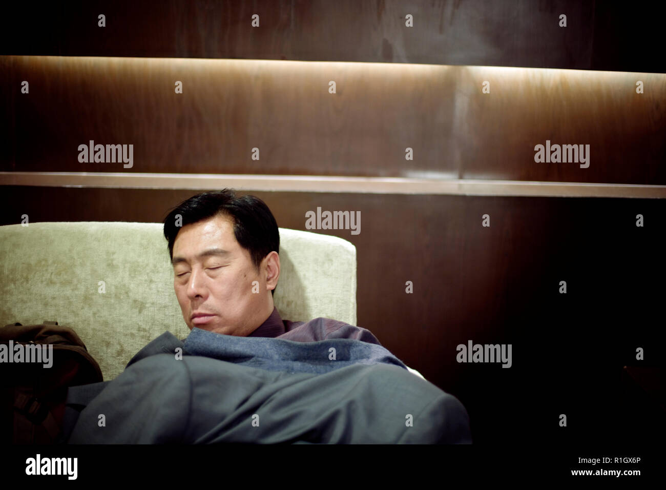 Metà di uomo adulto di dormire su una poltrona essendo coperto da una tuta giacca. Foto Stock