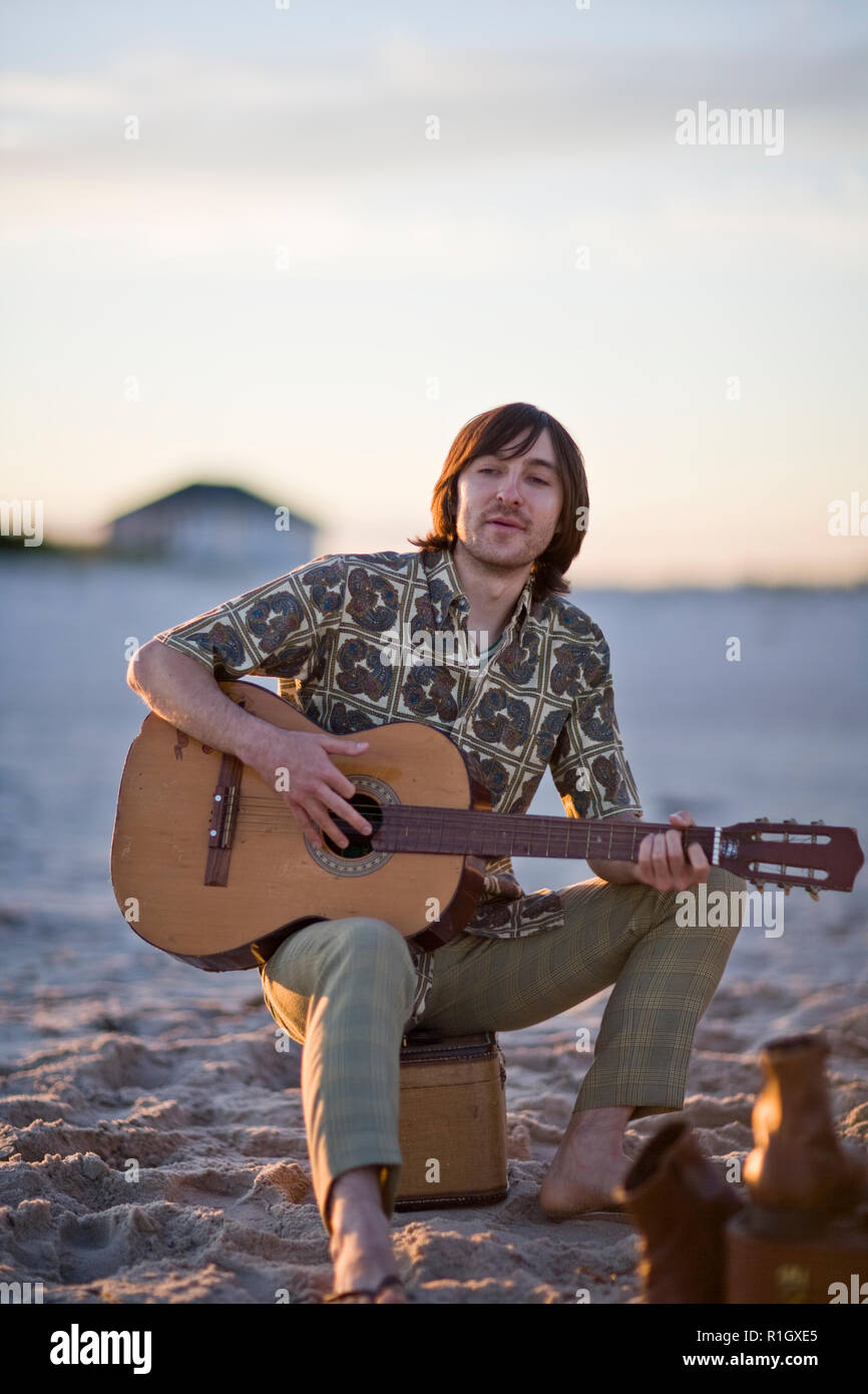 Giovane uomo di suonare una chitarra mentre è seduto su una spiaggia. Foto Stock