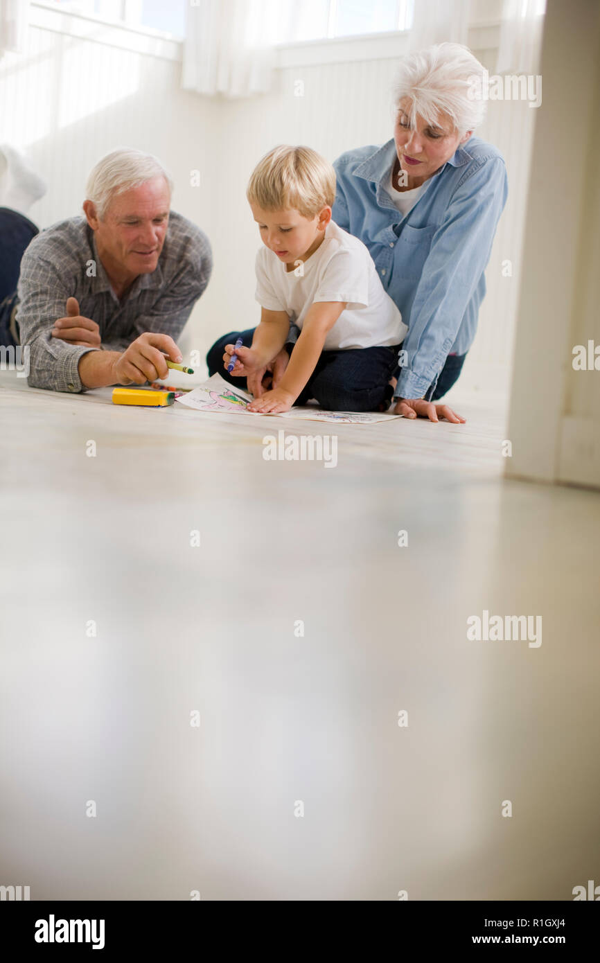 Ragazzo seduto sul pavimento con i suoi nonni e Disegno con matite colorate. Foto Stock