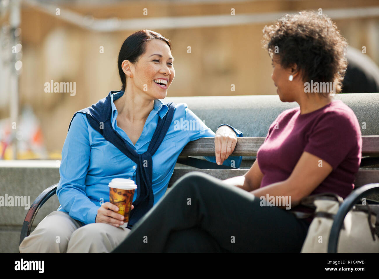 Due donne sorridenti avente un insieme di conversazione mentre è seduto in un parco della città. Foto Stock