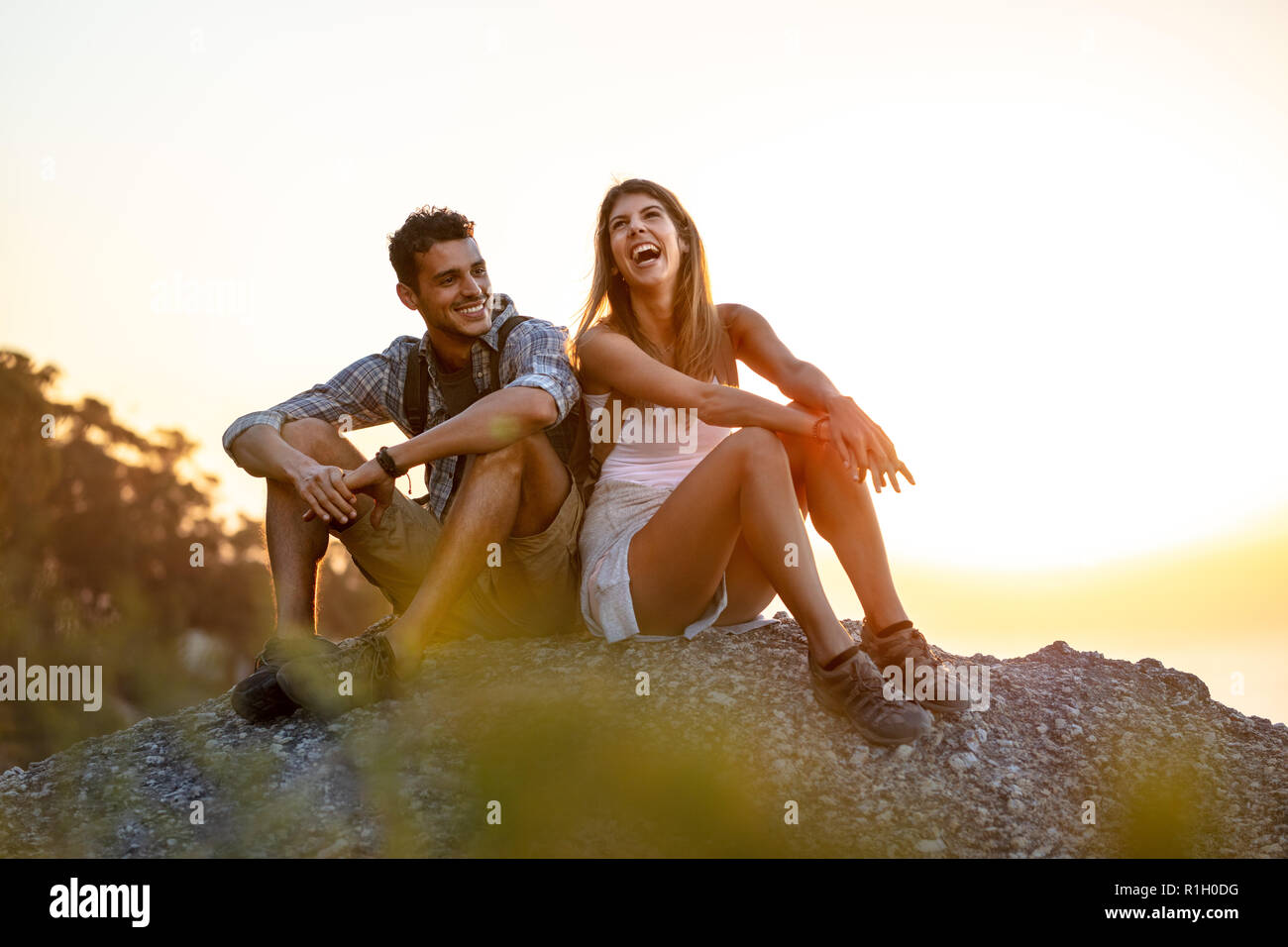 Coppia giovane prendendo una pausa durante un'escursione. Felice giovane uomo e donna seduta sulla cima della montagna e ridere. Foto Stock