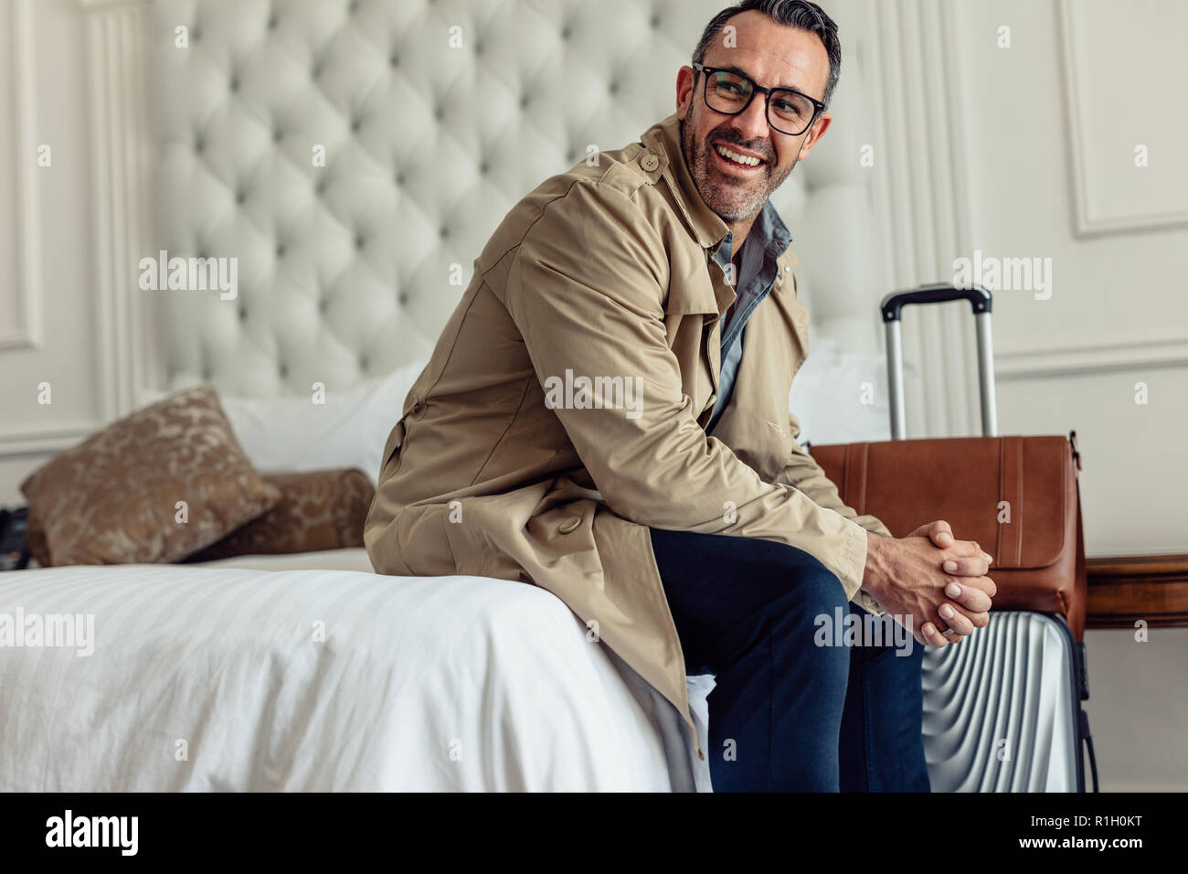 Imprenditore di successo con i bagagli seduto in camera di albergo bed e guardando lontano. Imprenditore maturo in viaggio d'affari. Foto Stock