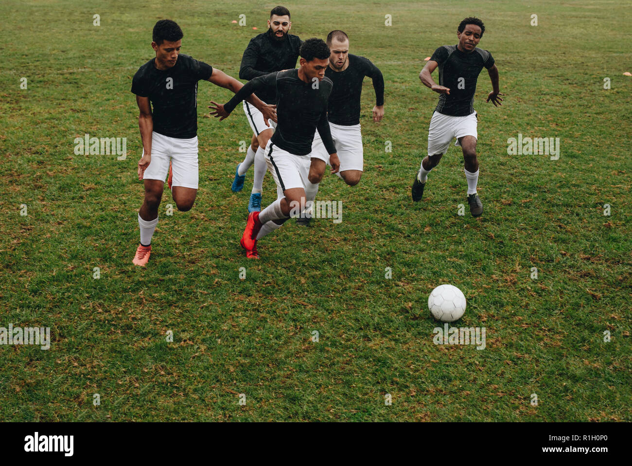 Un gruppo di uomini a giocare a calcio sul campo in esecuzione per la palla. I giocatori di calcio in esecuzione sul campo per il possesso di palla. Foto Stock