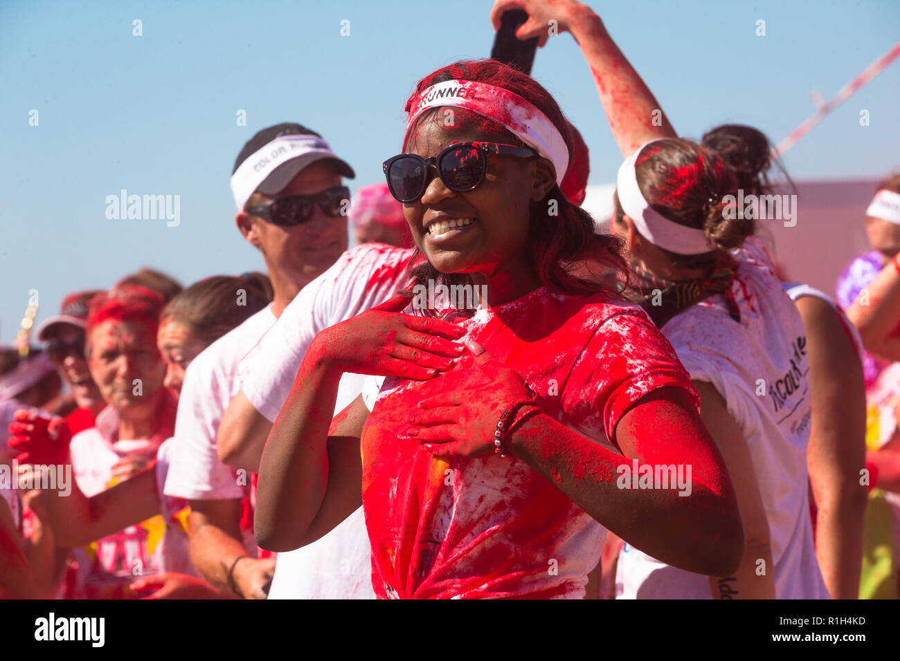 Africano nero lady donna o coperto di rosso vernice in polvere indossando occhiali da sole e fascia bianca che posano per una foto a fun run evento sportivo in estate Foto Stock