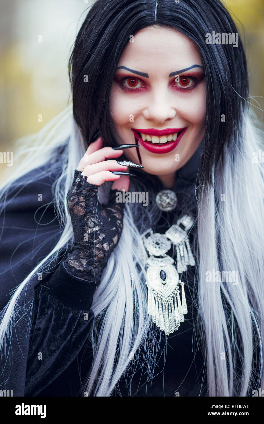 Ritratto di sorridente donna vampiro con il flusso di sangue in prossimità della bocca, occhi rossi in autunno park Foto Stock