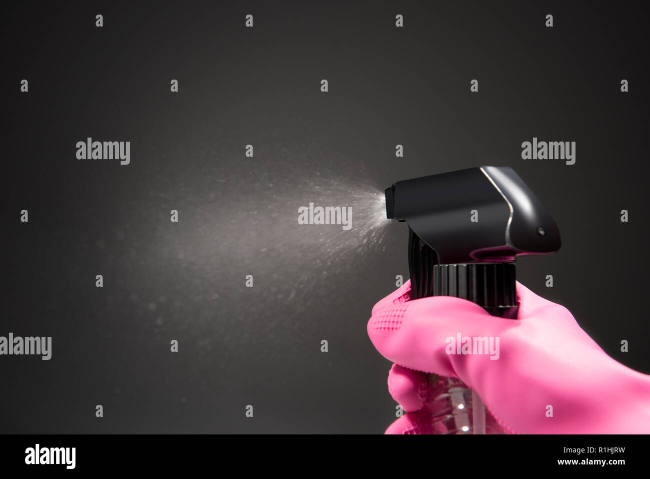 In mano i guanti utilizzando la bottiglia spray di spruzzatura di acqua nell'aria su sfondo nero Foto Stock