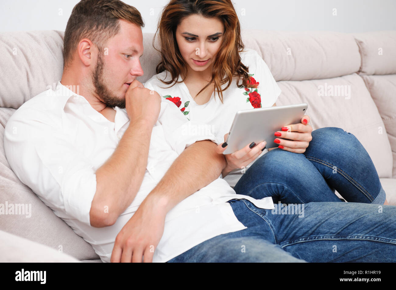 Famiglia giovane uomo e donna discutendo guardando a tavoletta digitale seduta in ambienti interni Foto Stock