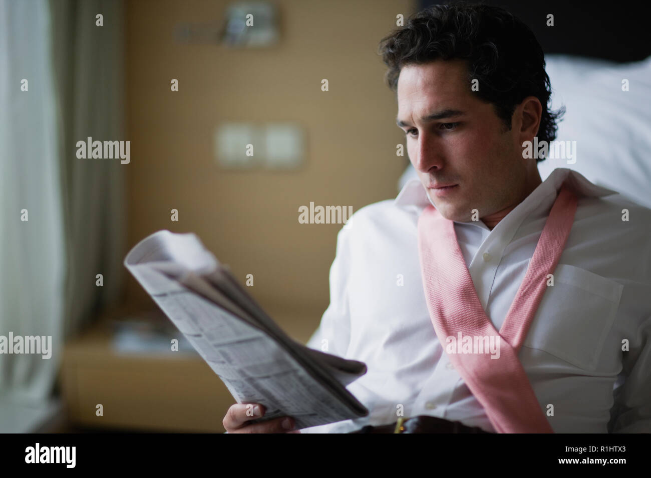 Giovane imprenditore leggendo un giornale all'interno di una camera di albergo. Foto Stock