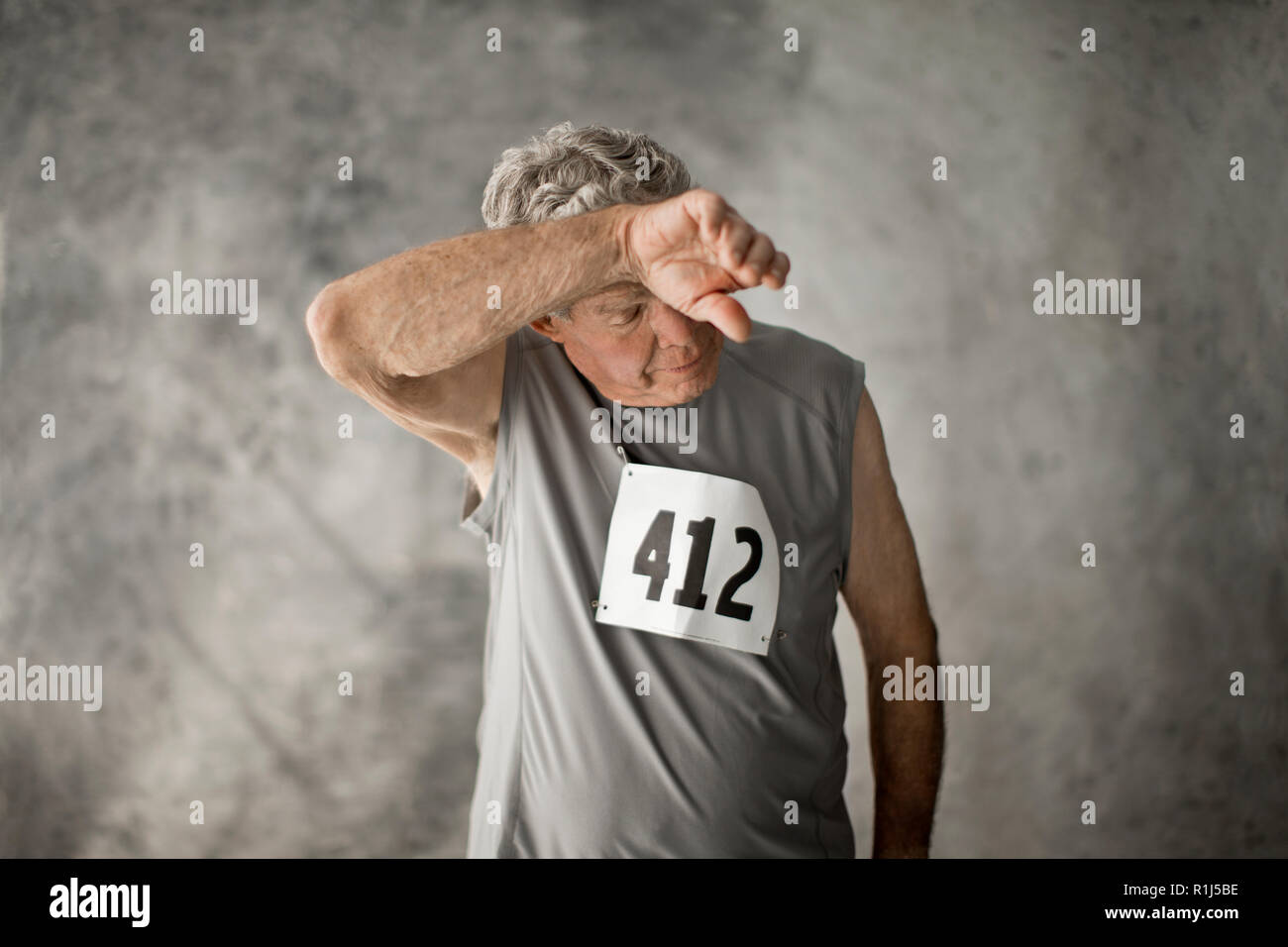 Stanco senior uomo strofinando il fronte con il suo braccio. Foto Stock