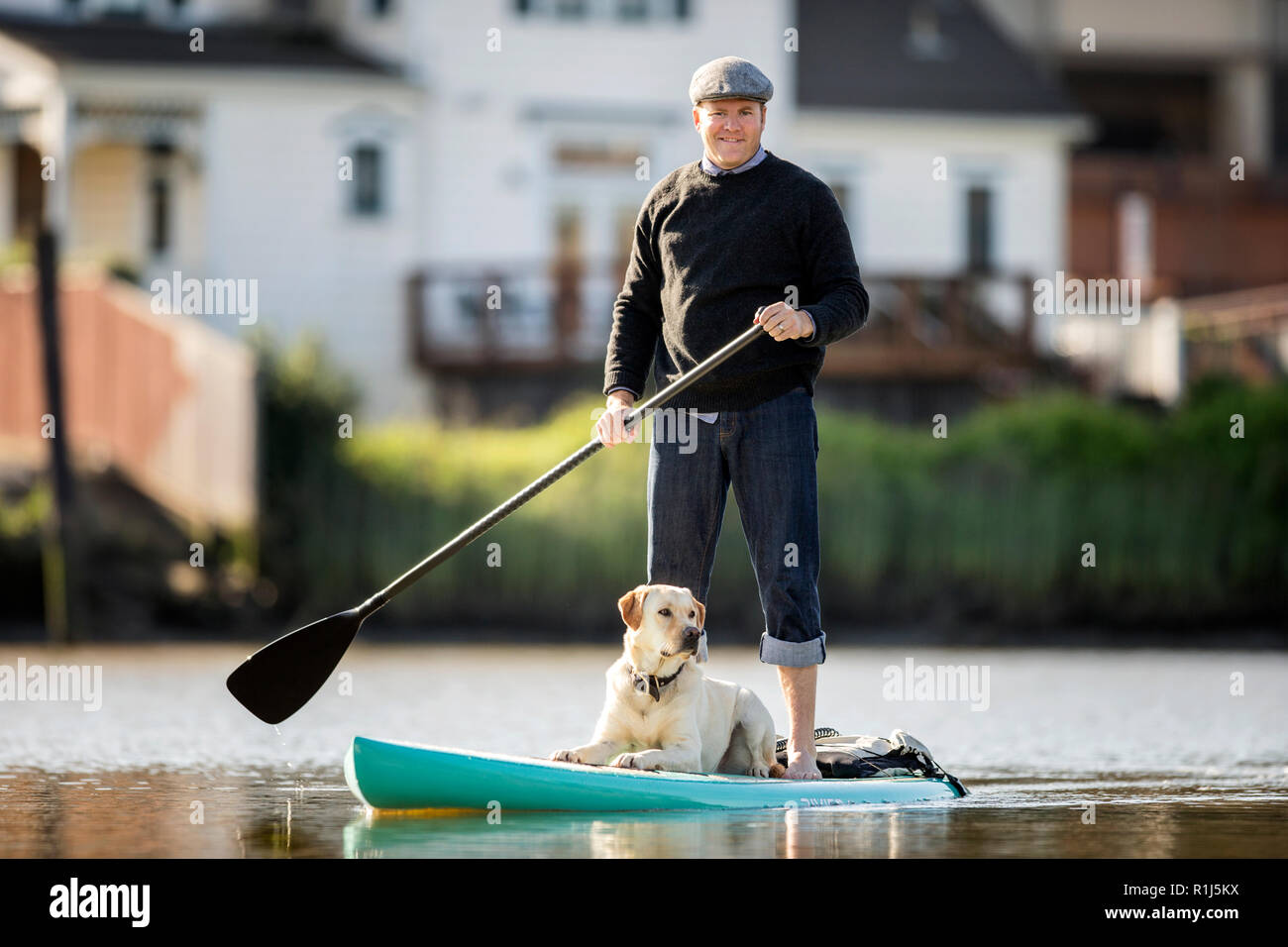 Uomo di mezza età paddleboarding sulle sponde di un lago con il suo cane. Foto Stock