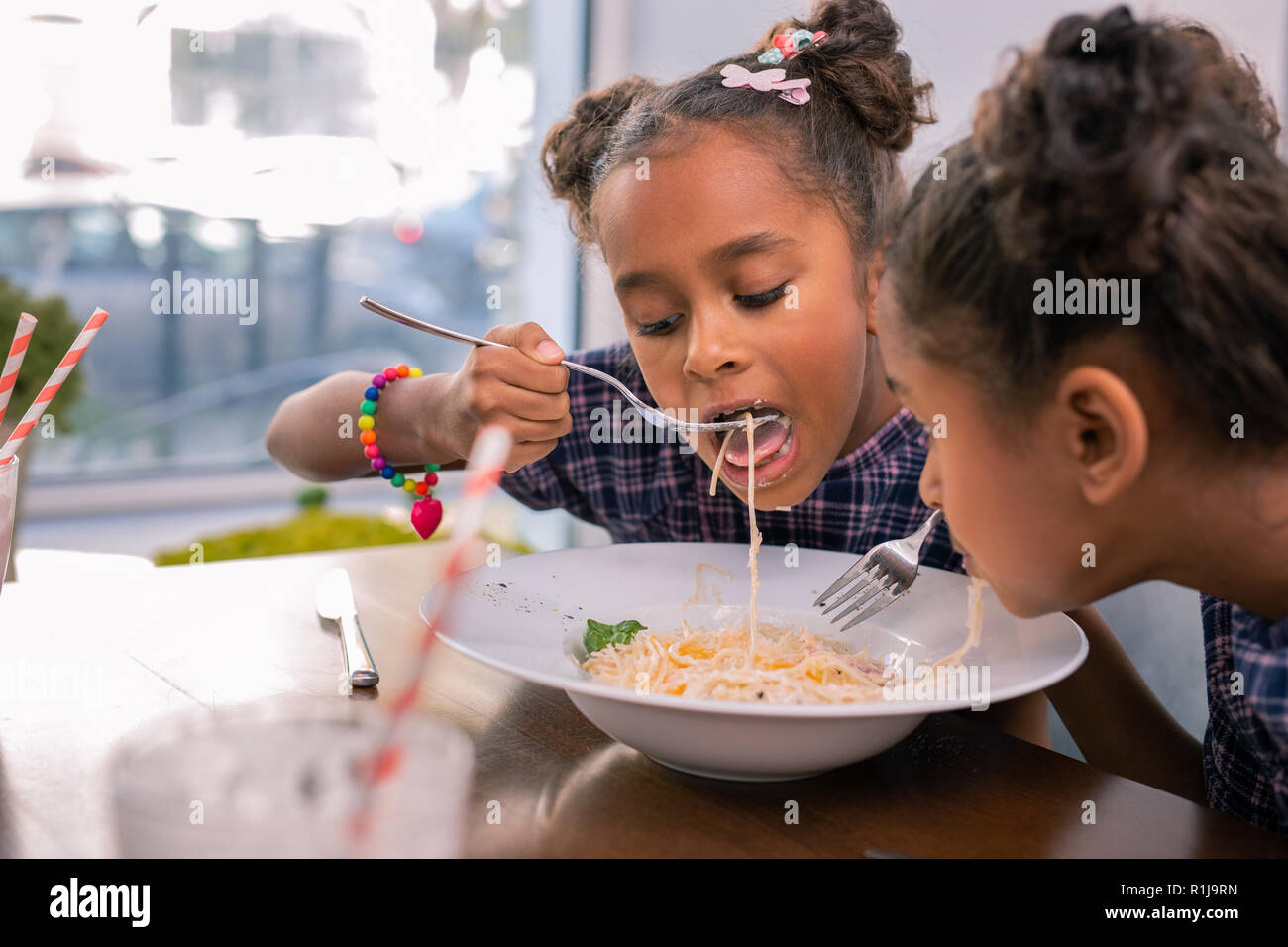 Carino bambina indossa un bracciale luminoso forcella di supporto e mangiare pasta Foto Stock