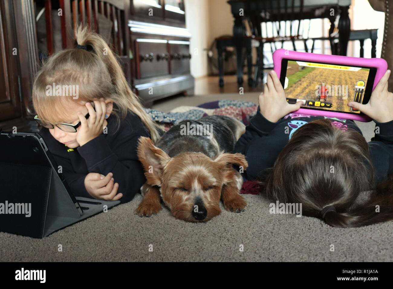 Sorelle che giocano ai videogiochi sui loro tablet con il loro migliore amico nelle vicinanze Foto Stock
