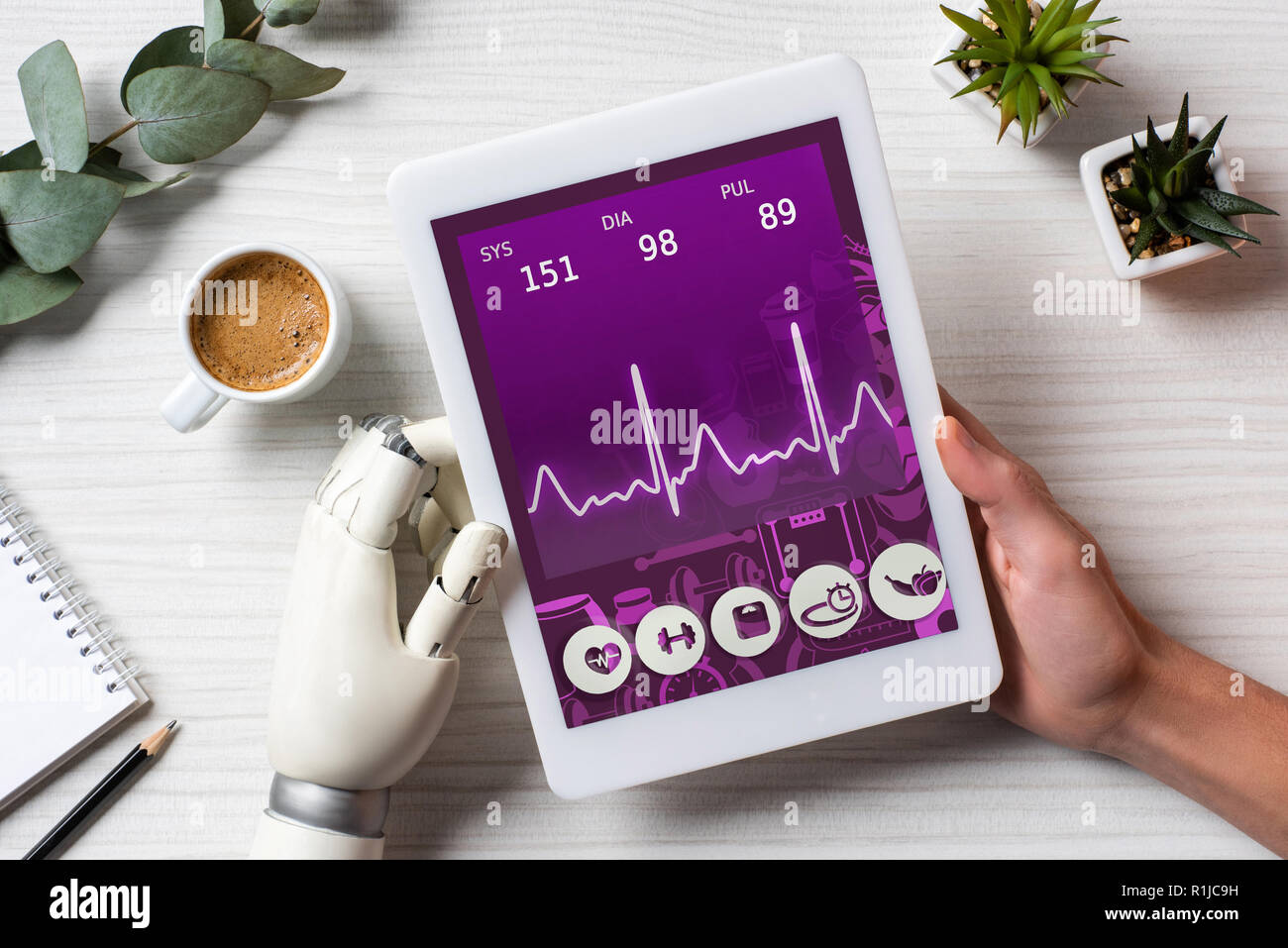 Immagine ritagliata di imprenditore con mano cyborg utilizzando tavoletta digitale con applicazione medica sullo schermo a tavola con la tazza di caffè in ufficio Foto Stock