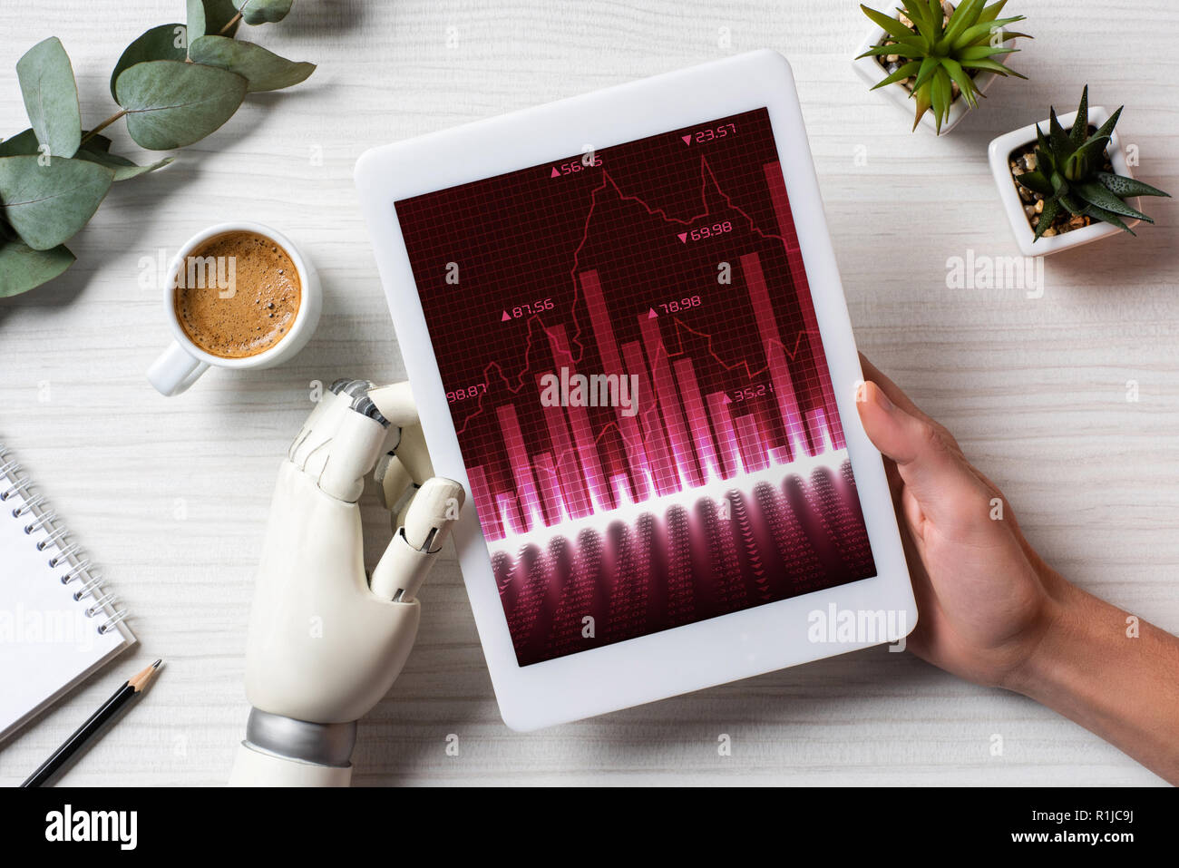 Immagine ritagliata di imprenditore con mano cyborg utilizzando tavoletta digitale con grafici a tavola con la tazza di caffè in ufficio Foto Stock
