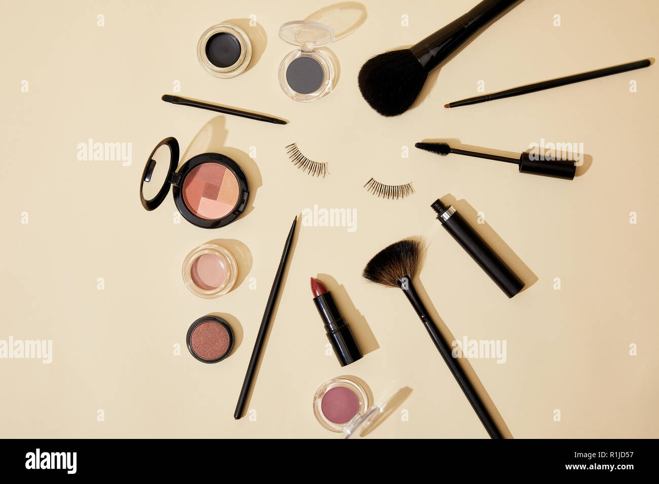 Vista dall'alto di diversi prodotti cosmetici giacente sulla superficie beige intorno a ciglia finte Foto Stock