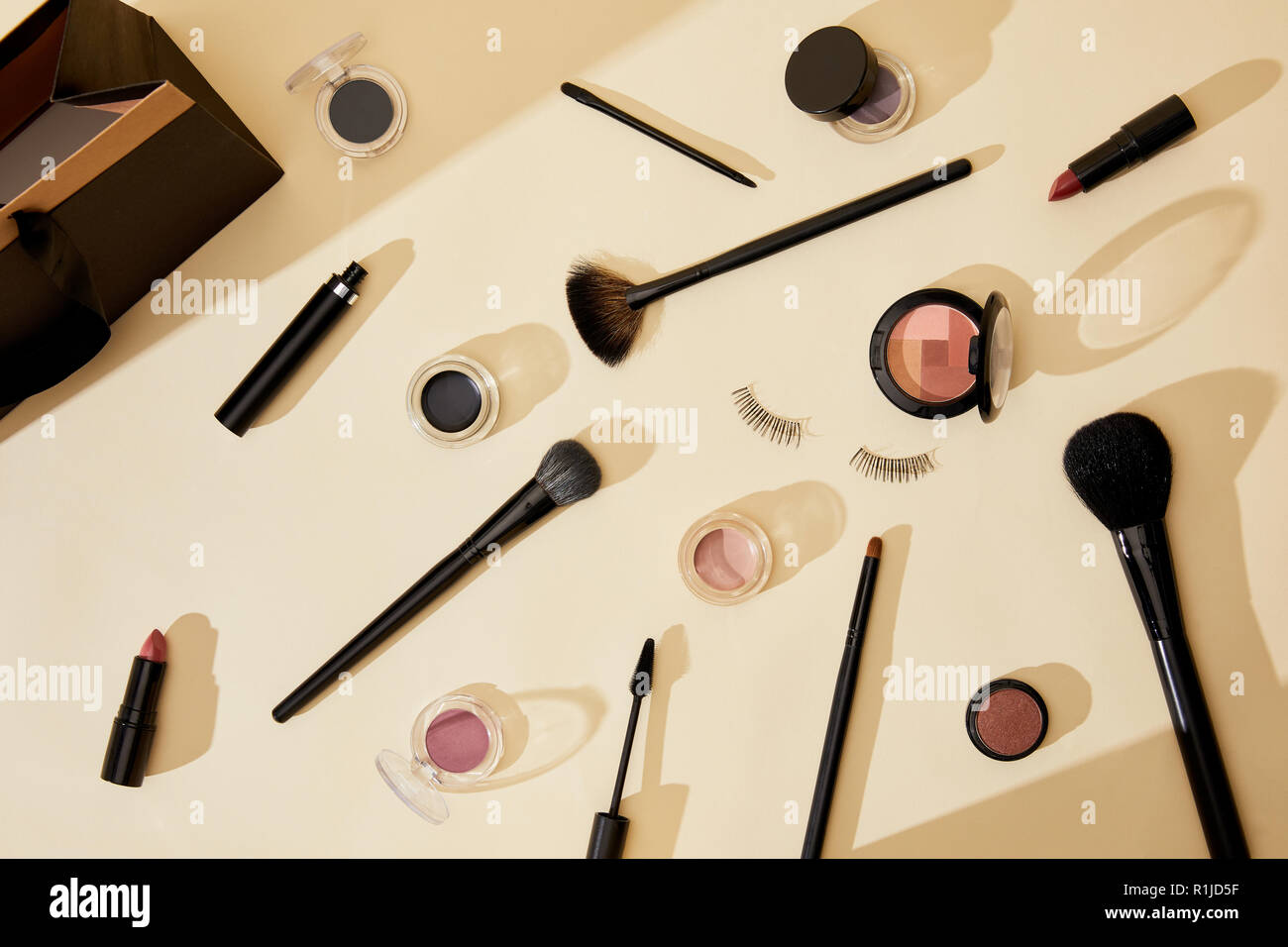 Vista dall'alto di diversi prodotti cosmetici e ciglia finte giacente sul piano portapaziente beige Foto Stock