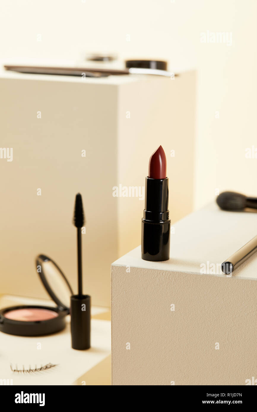 Close-up shot di rossetto rosso con vari accessori per il trucco su cubetti di colore beige Foto Stock