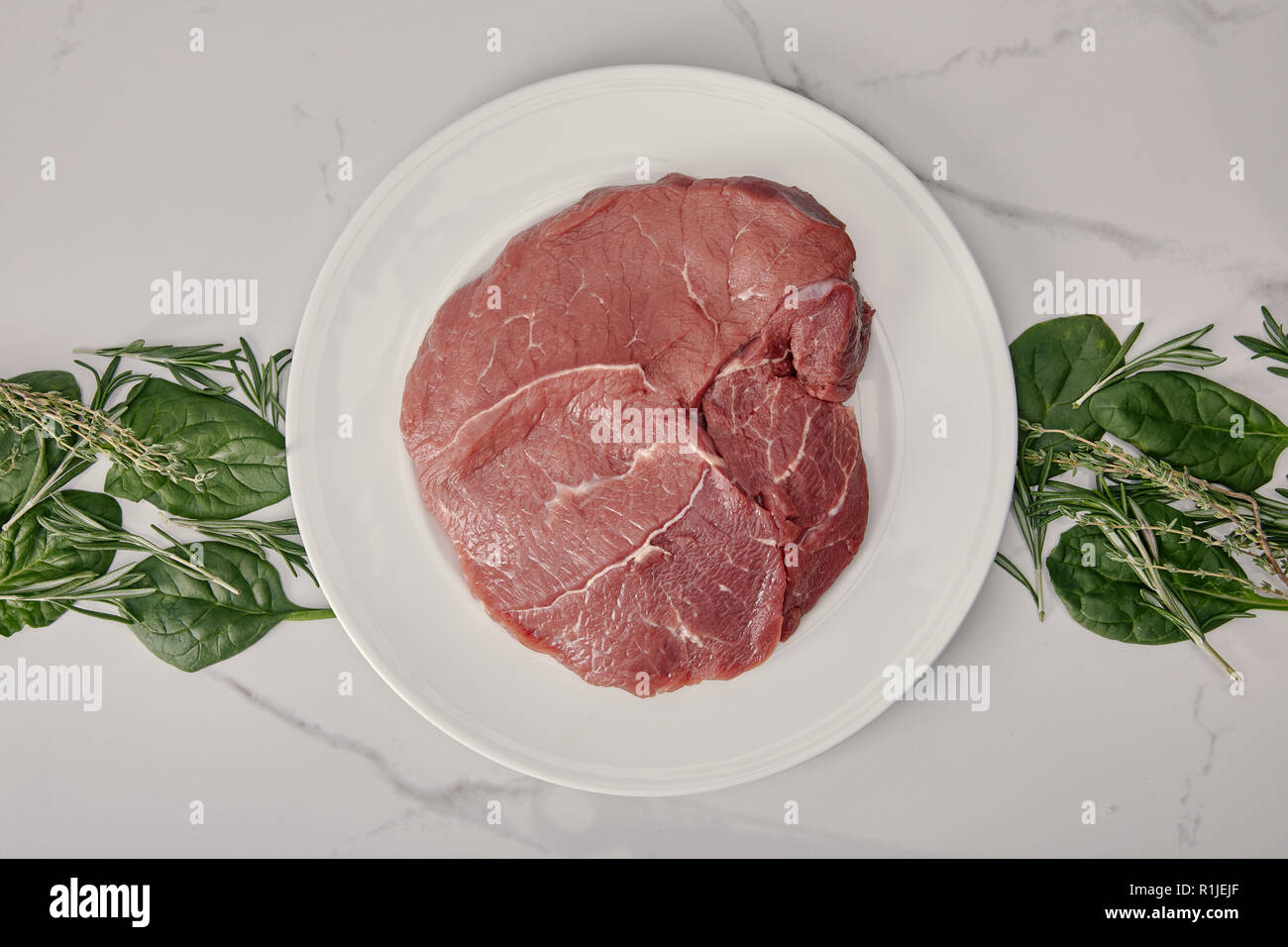 Vista dall'alto di carni la carne cruda sulla piastra con erbe su sfondo bianco Foto Stock