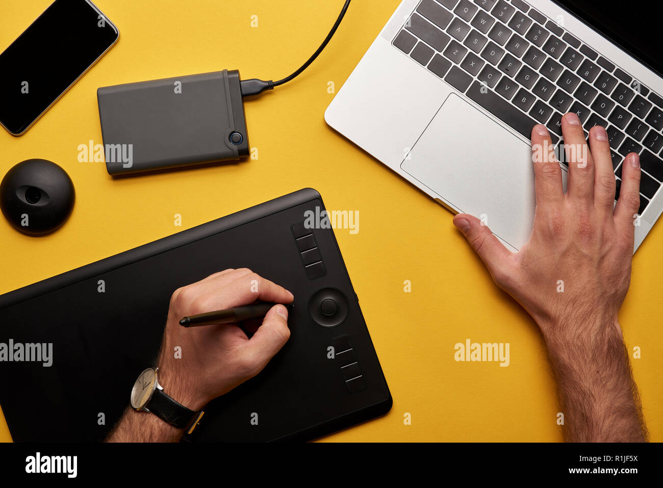 Ritagliato colpo di graphics designer che lavorano con il computer portatile e la tavoletta grafica sulla superficie gialla Foto Stock