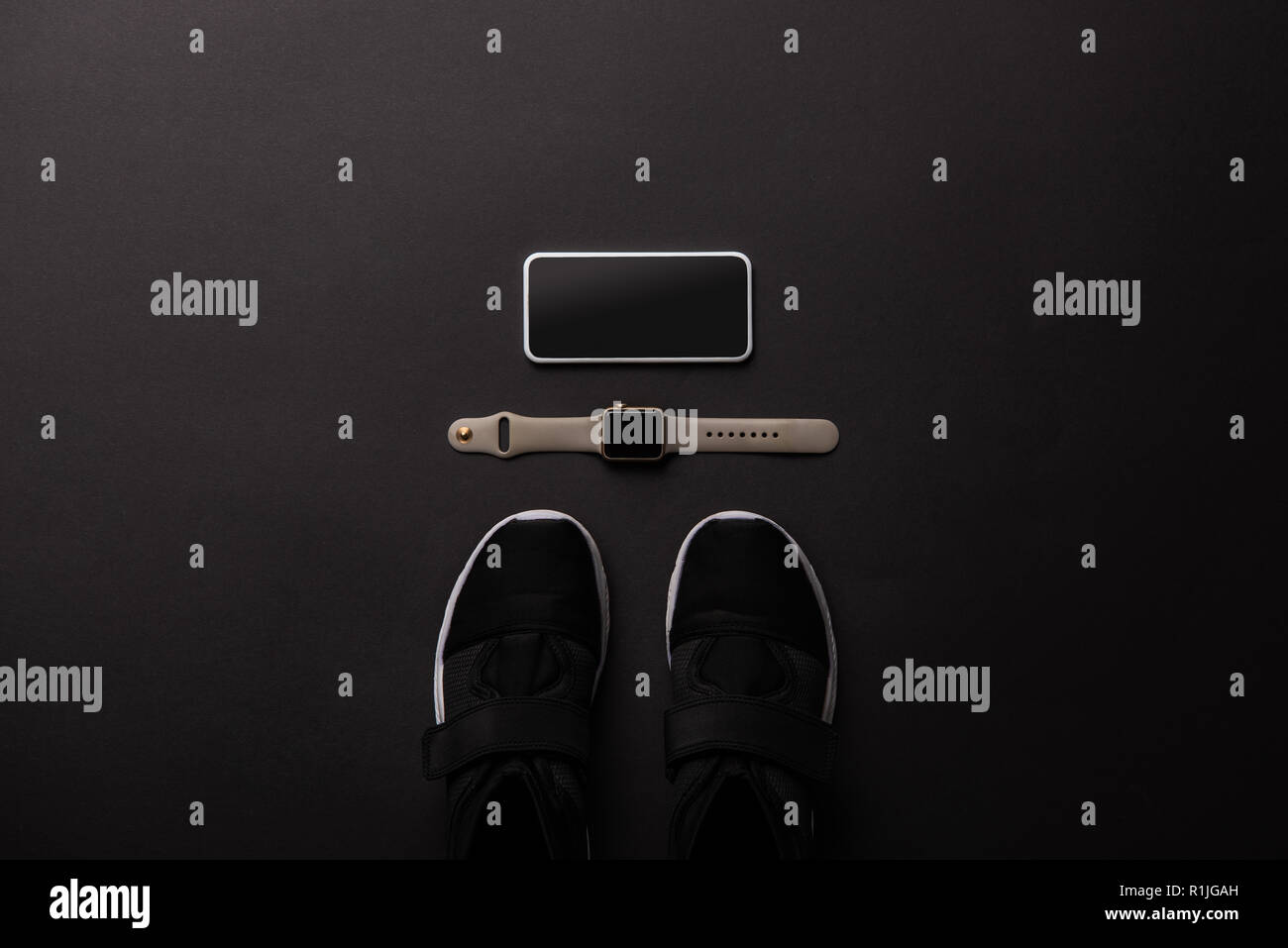 Piatto con laici disposti smartphone, smartwatch e sneakers isolato sul nero, concetto minimalista Foto Stock
