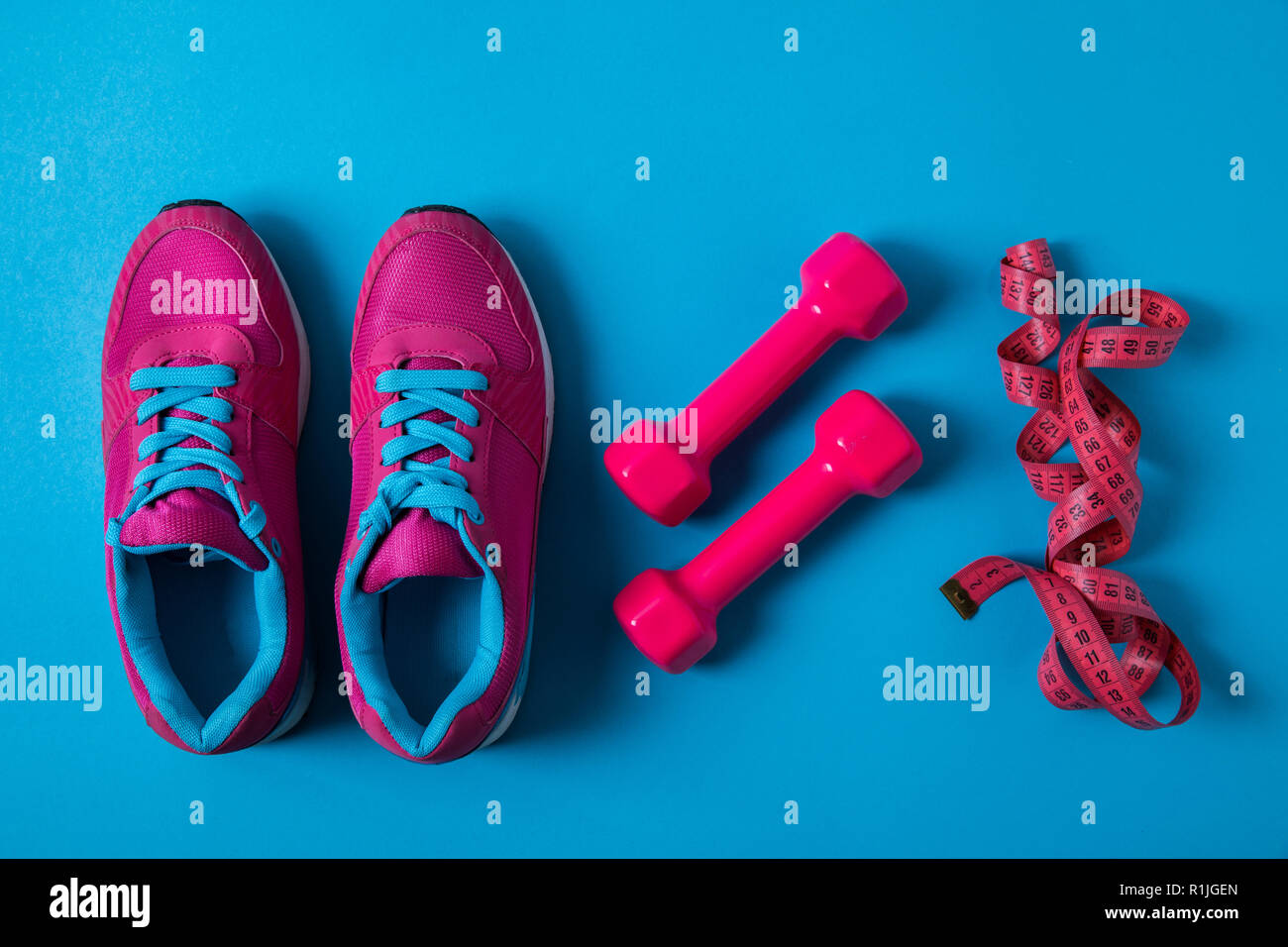Piatto con laici disposti rosa sneakers, pesi e nastro di misurazione posto nella riga isolata sul blu, concetto minimalista Foto Stock