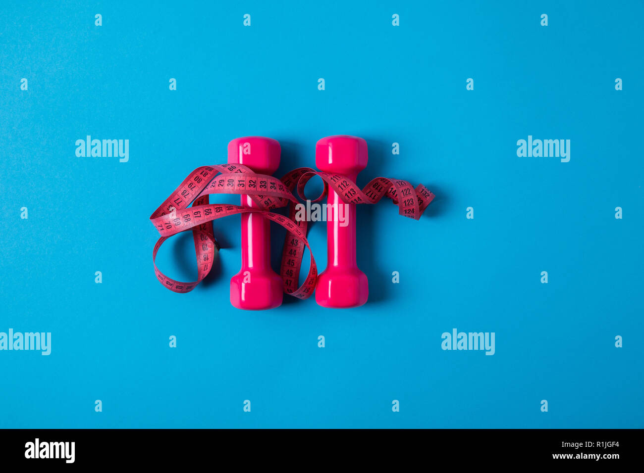 Appartamento laici rosa con nastro di misurazione e manubri isolato sul blu, concetto minimalista Foto Stock