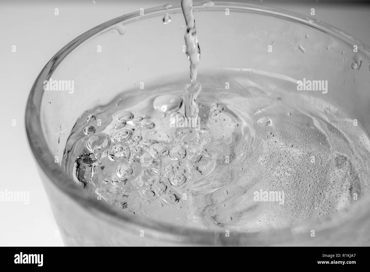 Versando acqua dalla bottiglia in vetro su sfondo bianco Foto Stock