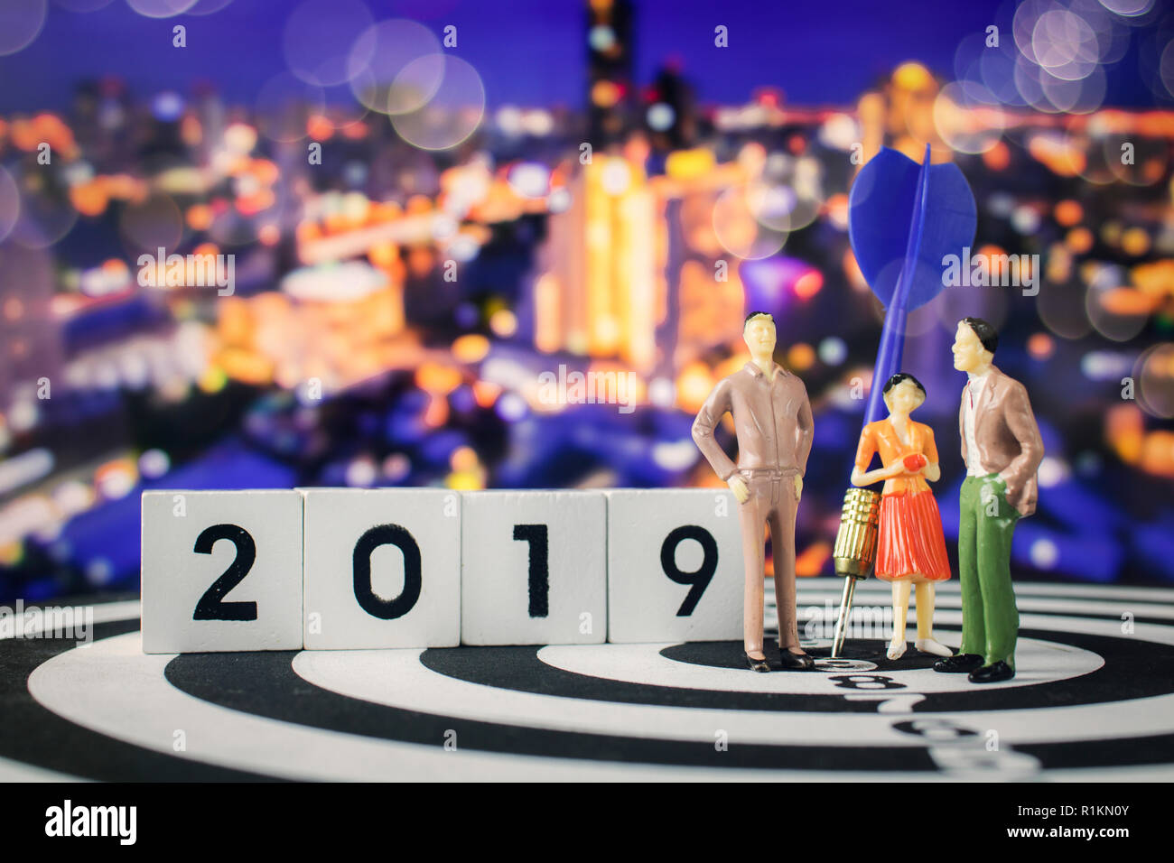 Obiettivo di business nel 2019, gruppo di persone cartoon parlando e piallare per obiettivo, permanente sulla scheda dart con night city sfondo bokeh di fondo Foto Stock