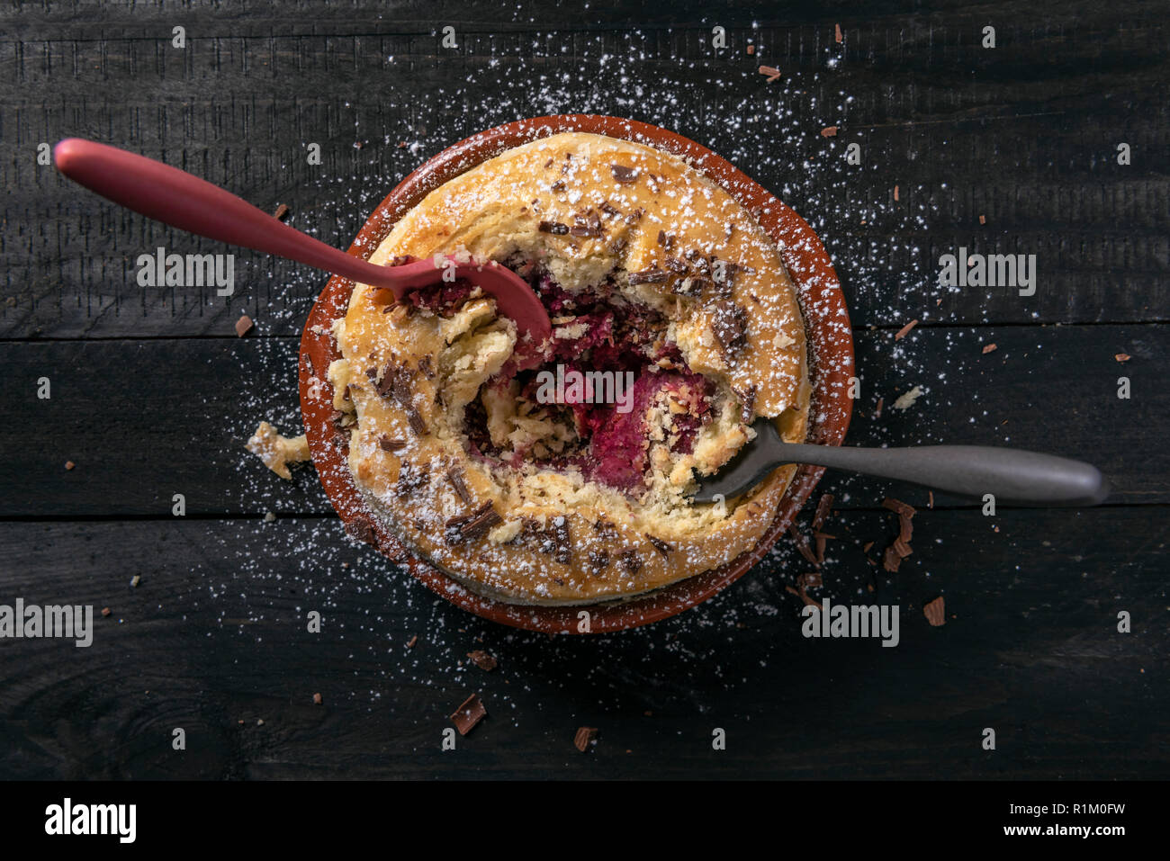 Direttamente sopra l'immagine di un lampone torta in una coppa in ceramica, con due cucchiai in esso, su un tavolo rustico. Divorando una torta salata. In casa la deliziosa torta. Foto Stock