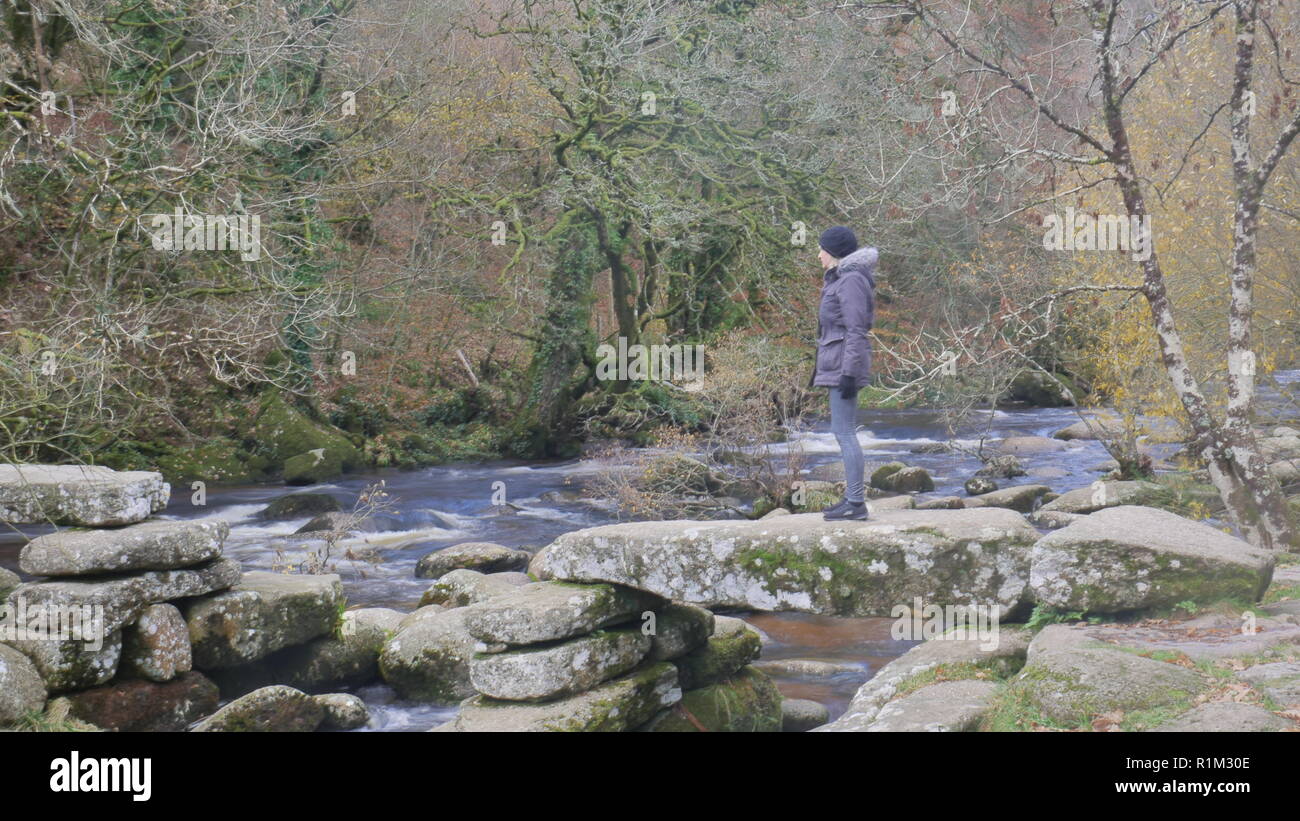 Baby Boomer bellissima femmina sorge sulle rovine di un battaglio ponte sul fiume Dart a Dartmeet Foto Stock