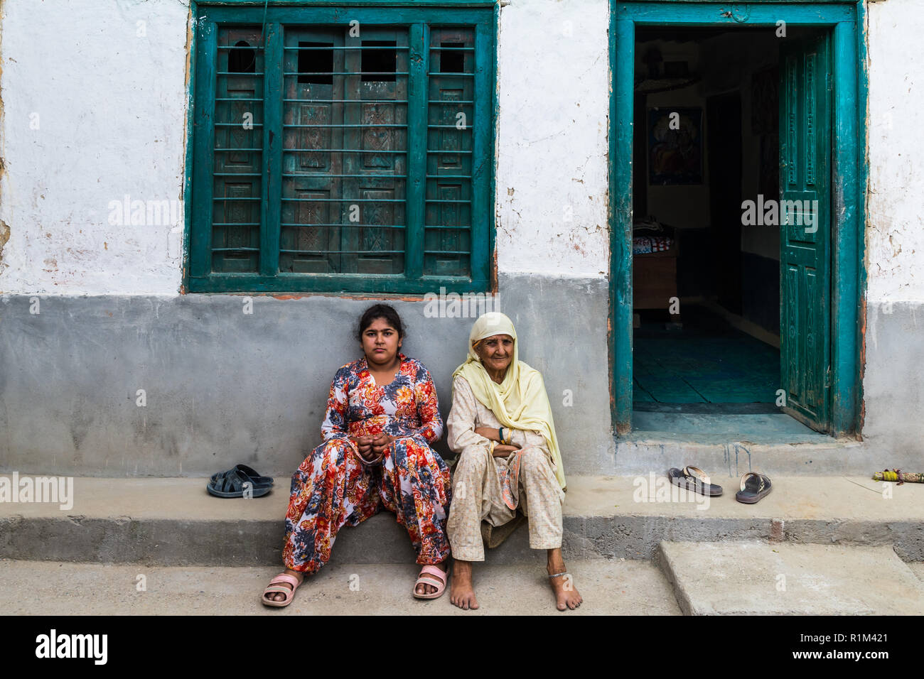 Nonna e sua nipote sono seduti sulla soglia di fronte alla porta della loro casa nel paese. Himachal Pradesh giugno 2018 Foto Stock