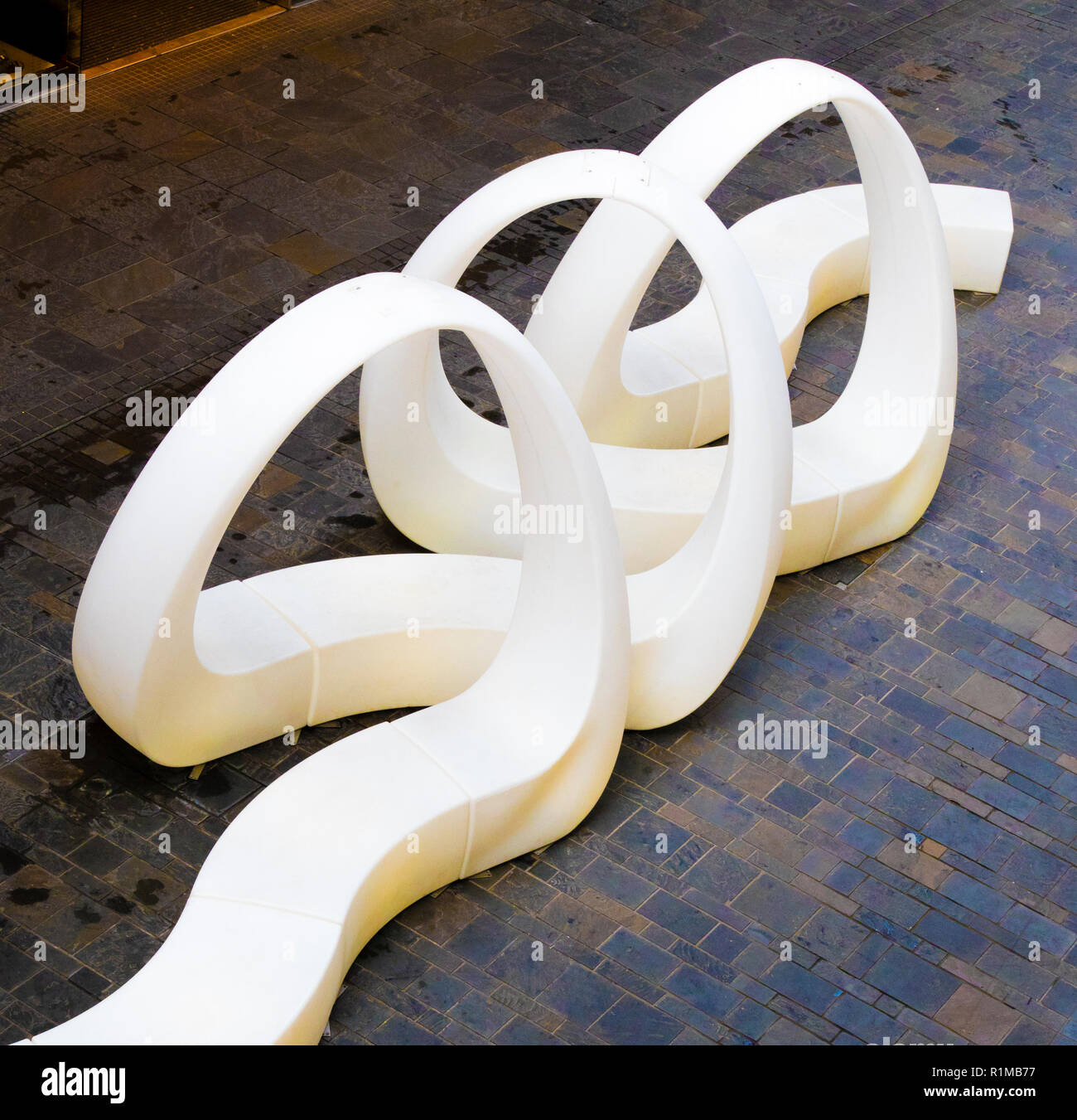 Una forma di pubblico posti a sedere in un quartiere dello shopping. Interessante ritorti e conformazione ad anello su di un pavimento piastrellato visto dal di sopra in Cabot Circus Bristol REGNO UNITO Foto Stock