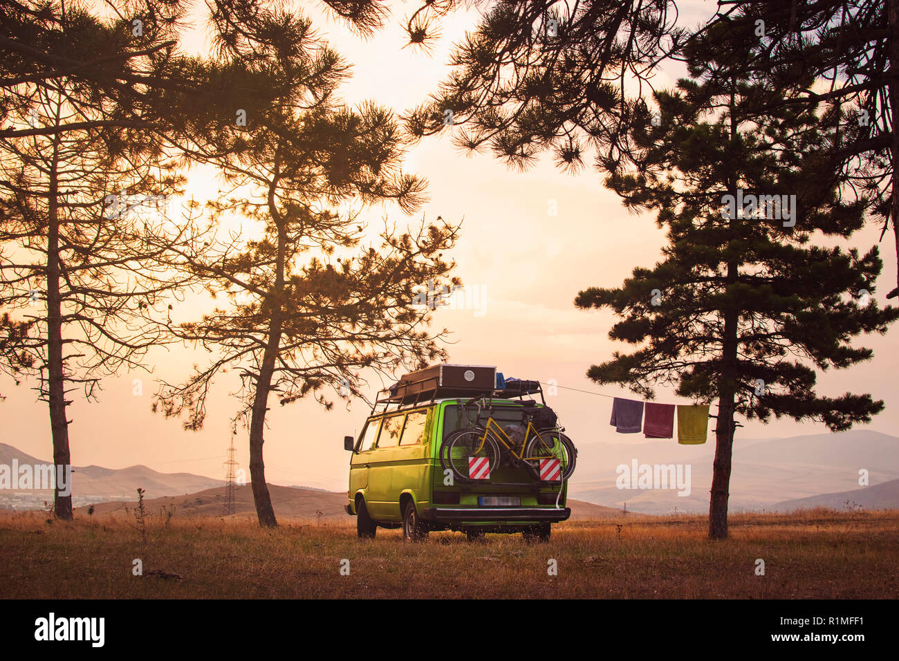 Old timer camper parcheggiato sulla cima della collina tra alberi di pino nel bel Cielo di tramonto Foto Stock