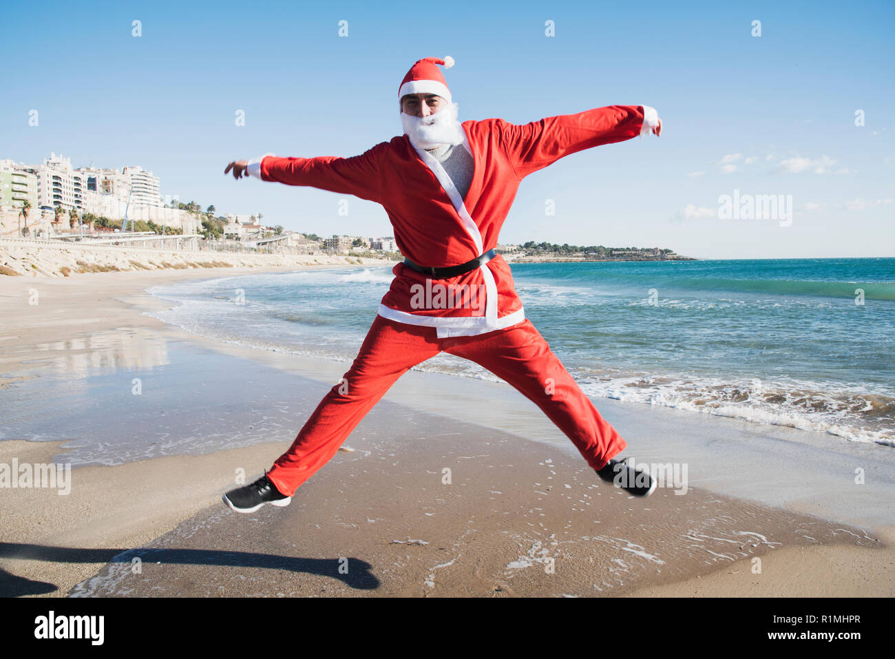 Un giovane uomo caucasico in una santa suit salta sulla spiaggia Foto Stock