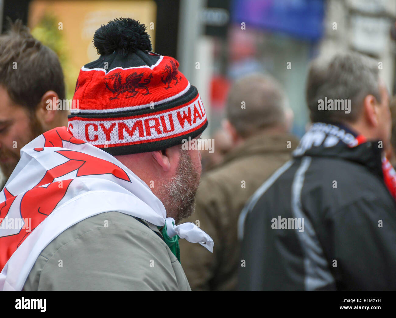 CARDIFF, GALLES - Novembre 2018: rugby gallese sostenitore con un bobble hat e una bandiera gallese, "drago rosso", drappeggiato sopra le spalle in Cardiff City Foto Stock