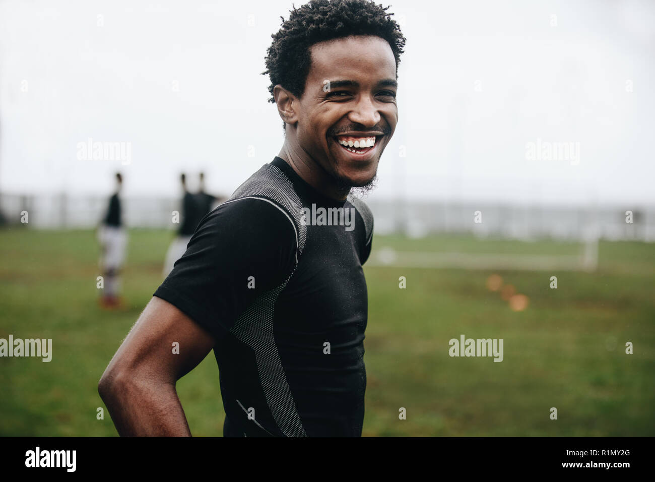 Ritratto di un allegro calciatore in piedi sul campo durante la pratica. Vista laterale di un africano giocatore di calcio in piedi sul campo di calcio la pratica in th Foto Stock