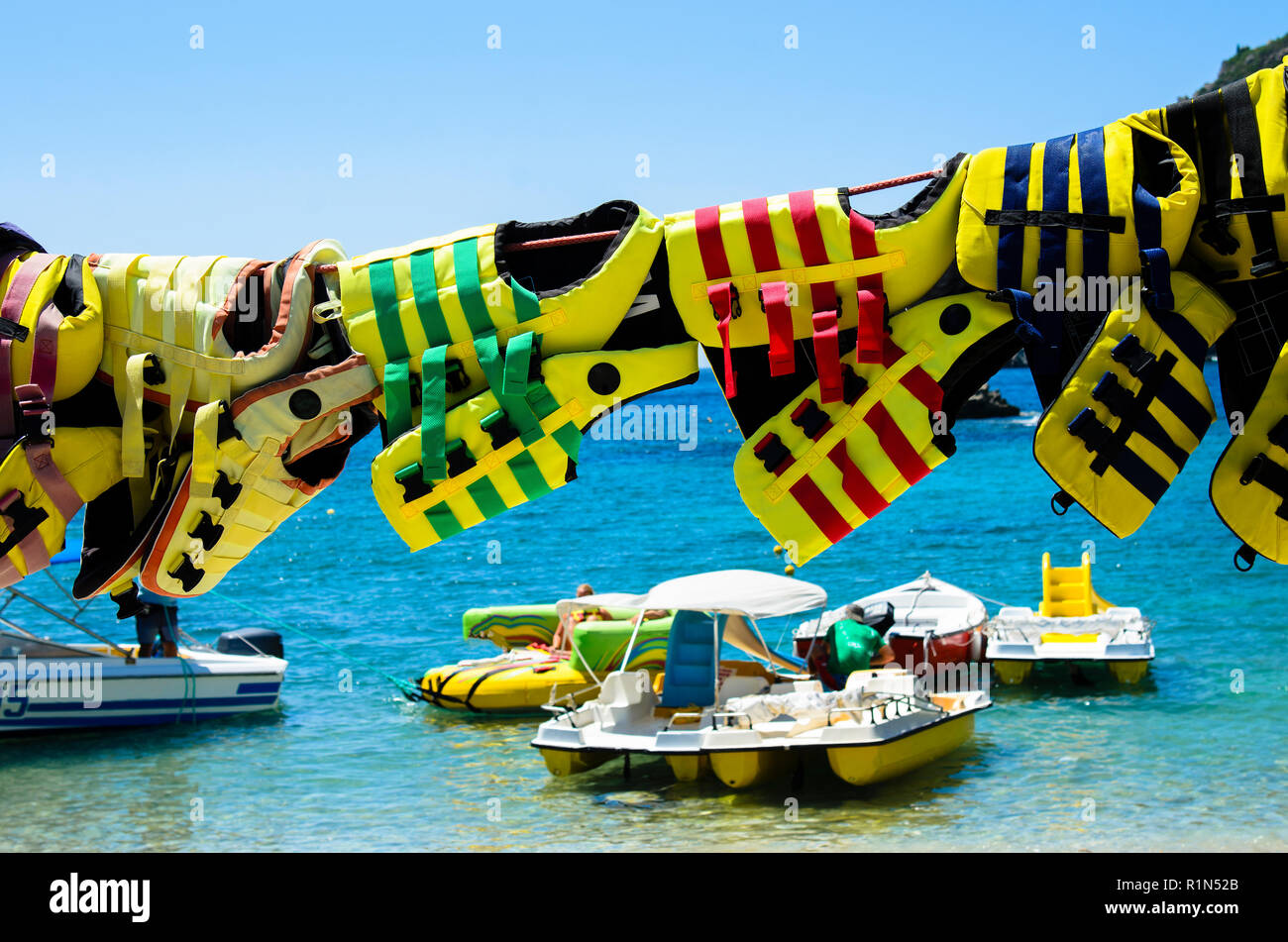 Giubbotti di salvataggio appesa ad asciugare sul fondo ormeggiati pedalò e barche, il cielo è blu e il mare turchese e verde Foto Stock